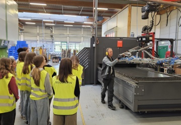 Die Schülerinnen bekommen beim Rundgang Einblicke in die Metallbearbeitung - hier stehen sie gerade neben der Laseranlage