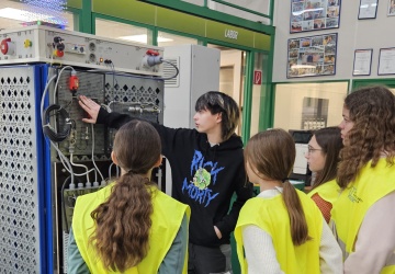 Schülerinnen erhalten gerade von einem weiblichen Lehrling die Pneumatik und Elektrotechnik vor einer Teststation erklärt