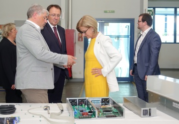 Die Gäste stehen im Geschäftsfeld Elektro beisammen und erhalten vom Geschäftsfeldleiter ein paar Informationen zu Produkten und Leistungen, am Bild sind auch mechatronische Bauteile zu sehen
