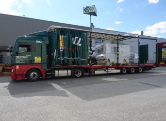 Ein dunkelgrüner LKW mit geöffneter Plane vor dem Gebäude der GW.