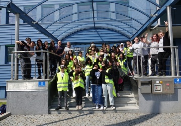 Gruppenfoto der Mitarbeiter*innen und Mädchen in Schutzwesten vor dem Haupteingang der GW