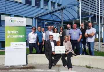 Gruppenfoto der Besucher*innen vor dem GW Gebäude, daneben ein RollUp mit 