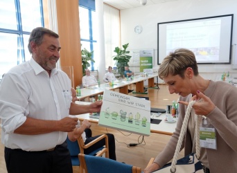 Ein Mann übergibt lächelnd eine Box an eine Frau, darauf steht 