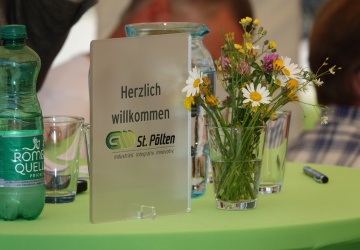 Ein Schild Herzlich Willkommen steht auf dem Rednerpult gemeinsam mit Blumen in einer Vase.