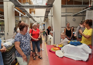 Gruppe von Gästen bei der Führung. Mittendrin sitzt ein Baby am Tisch und spielt sich mit den Gewichtstieren, welche ausgestellt sind.