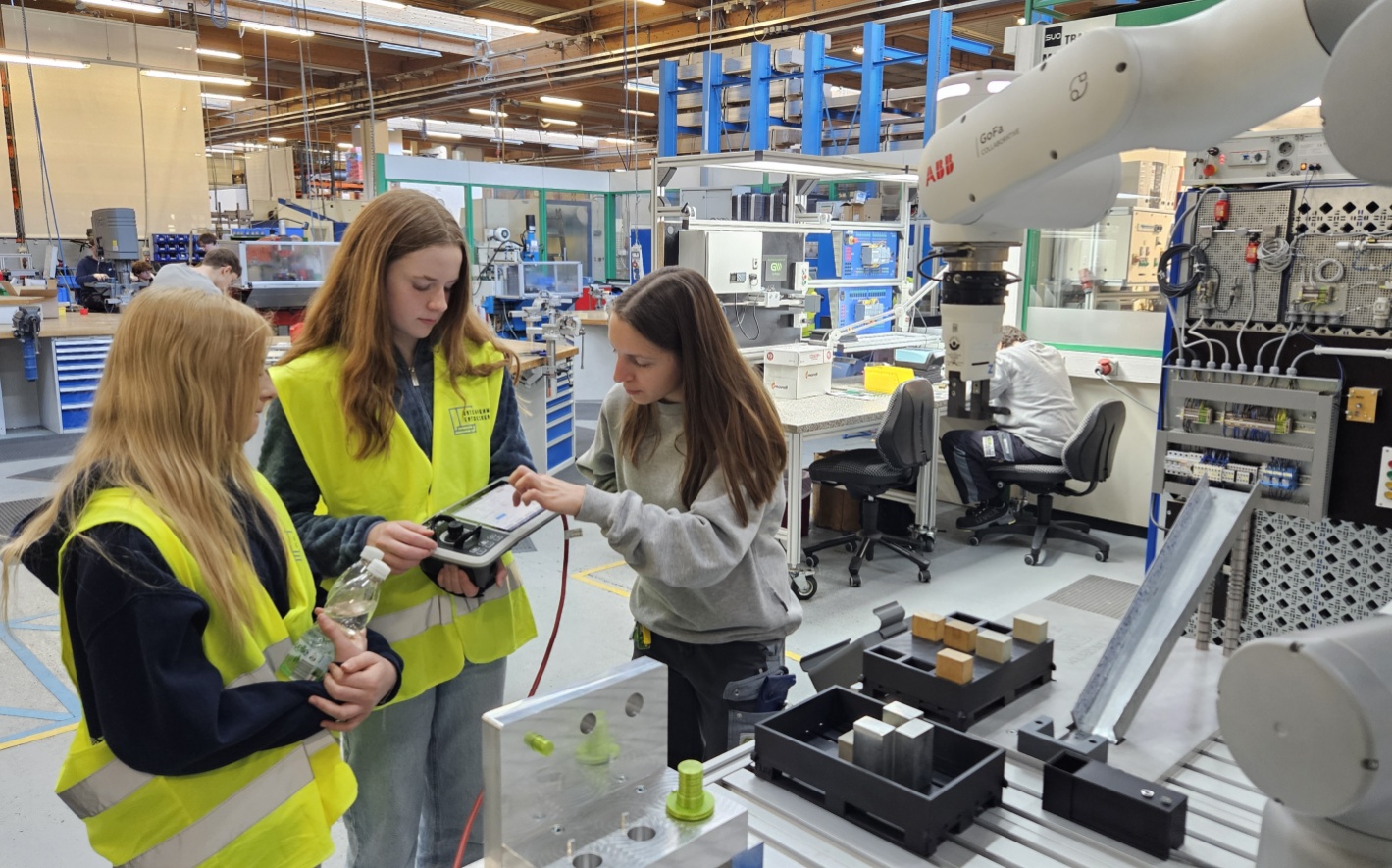 2 Schülerinnen dürfen gerade gemeinsam mit einem weiblichen Lehrling den Roboter ausprobieren