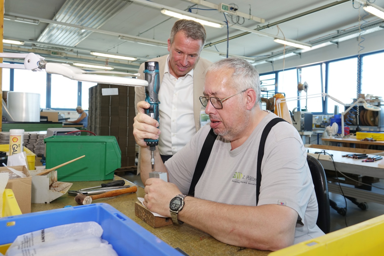 Dr. Johannes Kopf sieht einem GW-Mitarbeiter bei Montagetätigkeiten über die Schulter