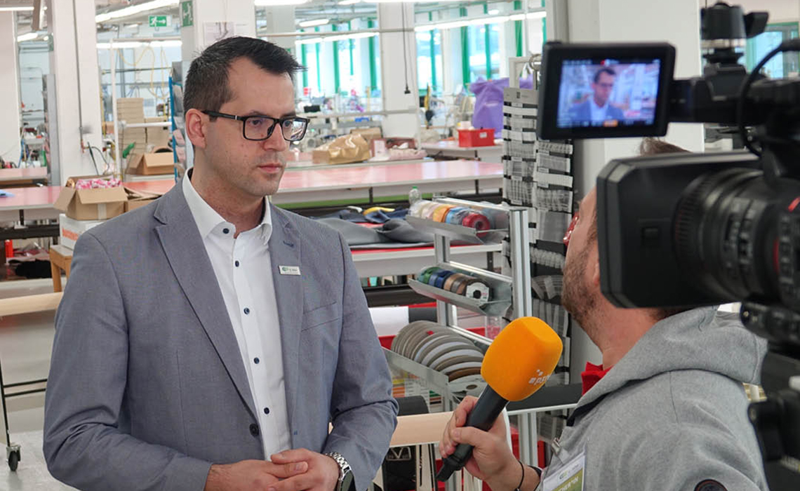 Ein Mann in grauen Sakko wird von einem anderen interviewt. Man sieht Teile einer TV-Kamera.