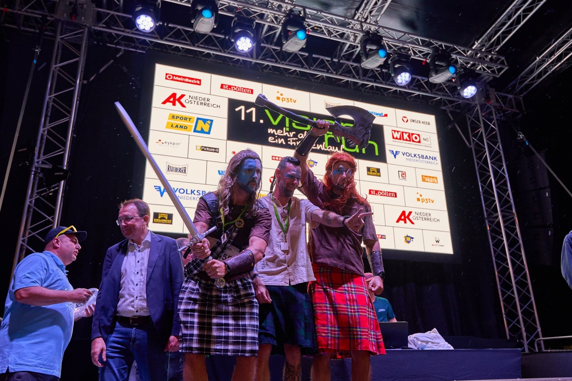 Gruppenfoto des 3er M&auml;nnerteams, sie haben den zweiten Platz erlangt und jubeln am Stockerl auf der B&uuml;hne