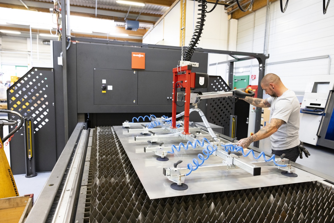 Foto der neuen Laseranlage - ein Mitarbeiter bedient gerade den Kran und hebt eine Metallplatte auf den Zufuhrtisch
