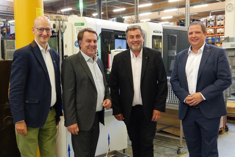 Vier Männer stehen lächelnd vor einer CNC Fräsmaschine.
