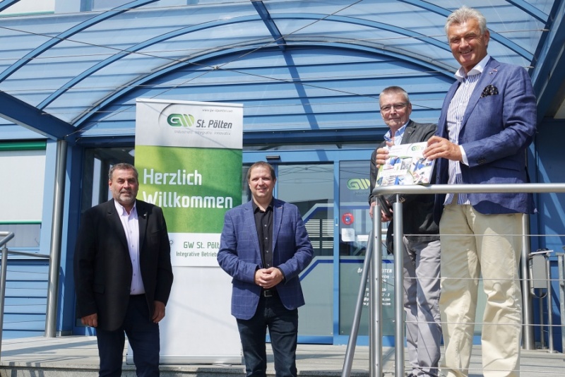 Gruppenfoto vierer Männer vor dem Eingang der GW. Dahinter ein RollUp mit dem Text "Herzlich Willkommen"