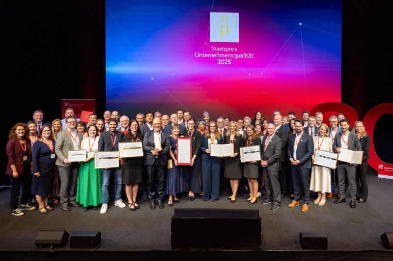 Auf dem Foto sehen Sie alle Finalist*innen zum Staatspreis Unternehmensqualität 2025 auf der Bühne - posierend für ein Pressefoto.