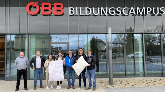 Gruppenfoto vor dem ÖBB Bildungscampus. Sie halten eine Decke und einen Polster in die Höhe.