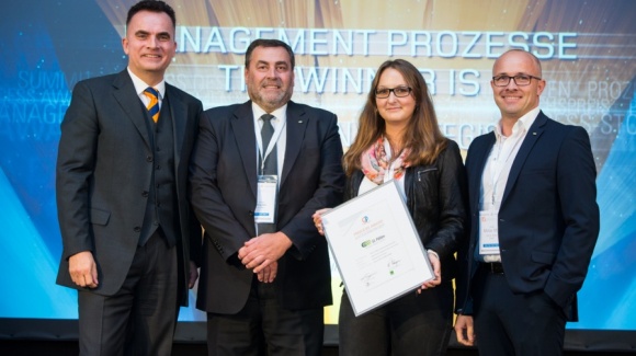 Gruppenfoto von 3 Männern und einer Frau mit dem Zertifikat vor einer bunten Wand.