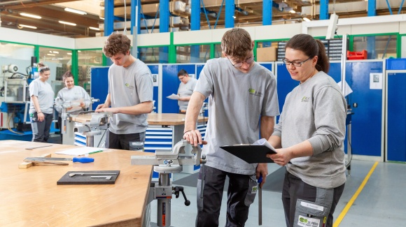 Foto aus der Lehrwerkst&auml;tte - es sind mehrere Lehrlinge bei der Arbeit zu sehen, weiters instruiert gerade eine Ausbilderin einen Lehrling
