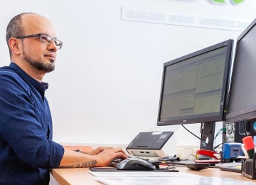 Mitarbeiter sitzt an einem B&uuml;roarbeitsplatz mit zwei Monitoren und arbeitet am Computer.