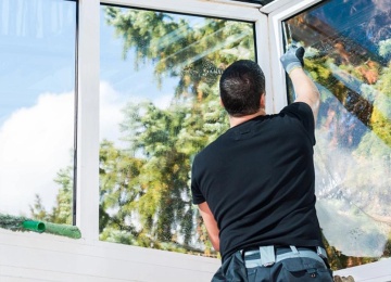 Mitarbeiter reinigt die Au&szlig;enseite eines gro&szlig;en Fensters mit einem Einwascher und einem Abzieher.