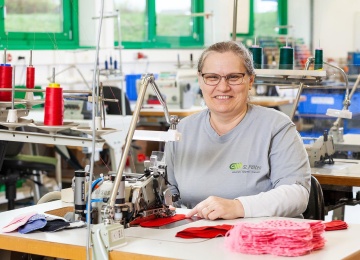Mitarbeiterin sitzt an einer Industrien&auml;hmaschine und verarbeitet Stoff in einer Textilwerkstatt.