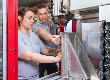 Lehrlingsausbilder erkl&auml;rt dem Lehrling wie man die CNC-Fr&auml;smaschine am Werkst&uuml;ck bedient.