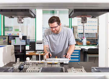 Junger Mann in grauen Shirt steht konzentriert vor einer Metallverarbeitungsmaschine.