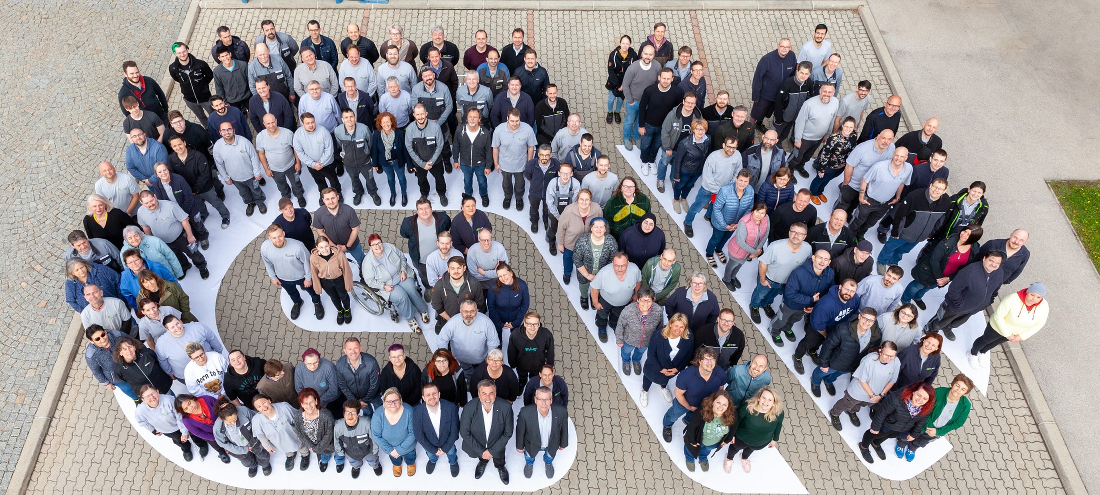 Eine Gruppe Menschen bildet den Schriftzug GW und blickt von unten in die Kamera hinauf.