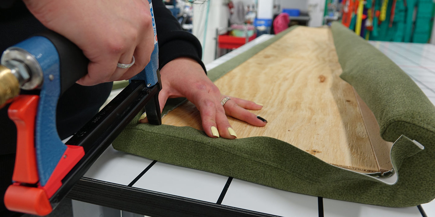 Man sieht zwei Hände bei Polsterarbeiten - es wird mit einem Handtacker gearbeitet.