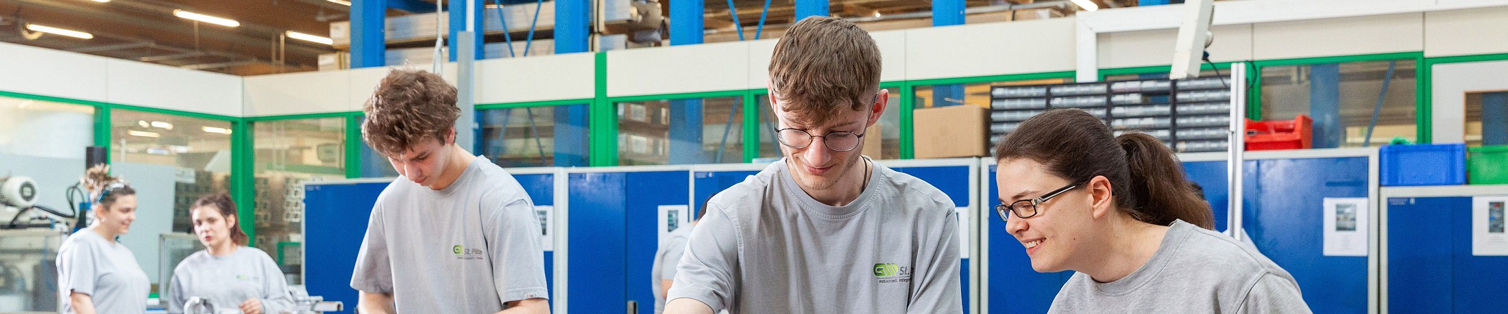 5 junge Menschen stehen in einer Lehrwerkstätte und arbeiten.