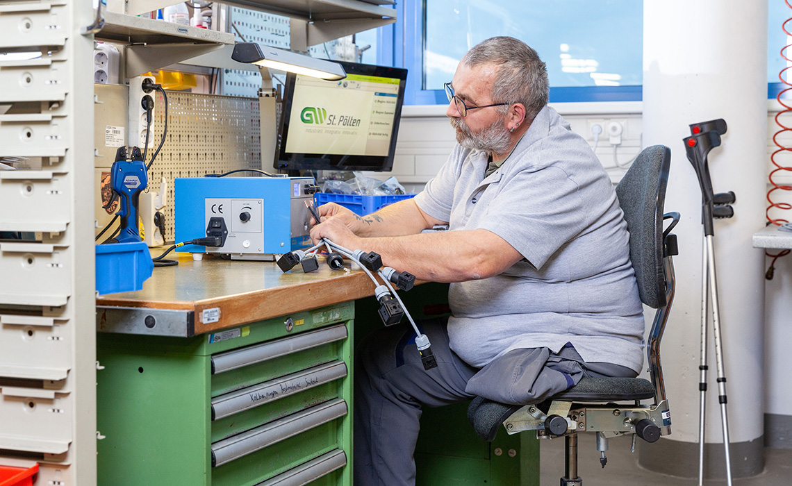 Mann mit einem Bein sitzt an Arbeitsplatz und bearbeitet Elektroteile.