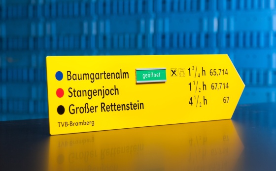 Auf dem Bild sieht man einen fertigen Wanderwegweiser in gelber Farbe mit Aufschrift.
