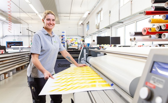 Junge, blonde Frau arbeitet an einer Folien-Druckmaschine.