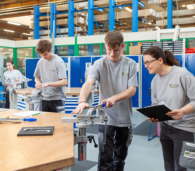 4 Personen stehen in einer Werkstätte und arbeiten/ besprechen Werkstücke.